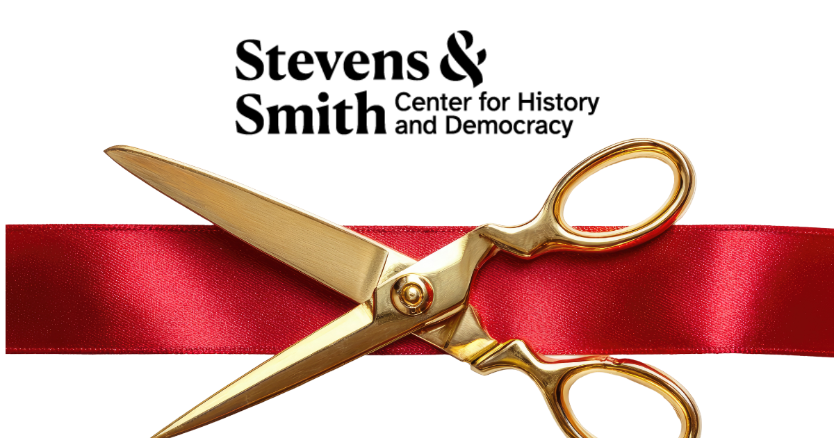 A pair of gold scissors lays on top of a bright red fabric ribbon.